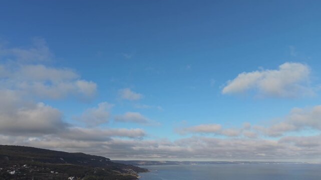 Aerial drone footage capturing wide open blue sky with soft scattered clouds drifting slowly, creating peaceful atmospheric scenery and natural daylight patterns in a calm and serene outdoor environme