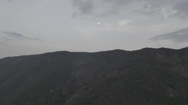 Aerial view of lush green Aravali hills near Pushkar, Rajasthan during evening, with the moon rising behind scattered clouds, capturing serene rolling hills and natural beauty from above.