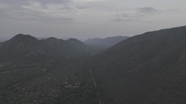 Aerial view of lush green Aravali hills near Pushkar, Rajasthan during evening, with clouds drifting across the sky, capturing the serene landscape, rolling hills, and natural beauty from above.