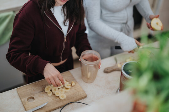 Two women are in a kitchen preparing a smoothie with fresh fruits, showcasing a healthy lifestyle, teamwork, and nutritious food preparation, promoting wholesome and vibrant living.
