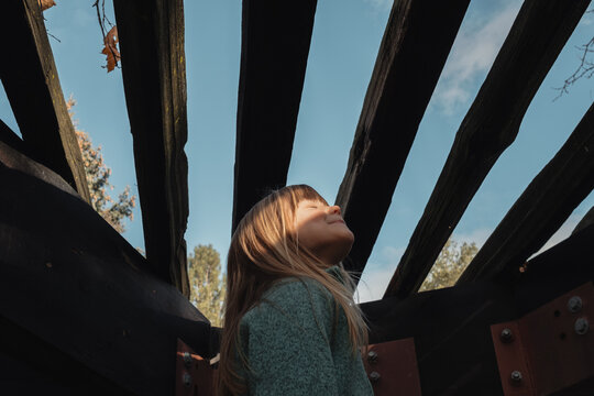Young girl looking up at sunshine through wooden beams