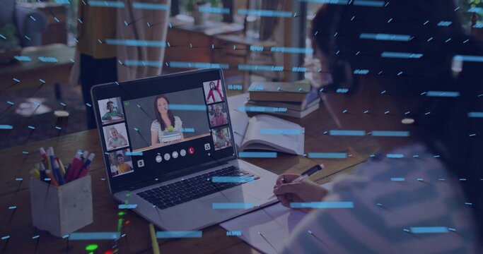 Writing teacher wearing striped top noting in notebook at home with laptop and pen