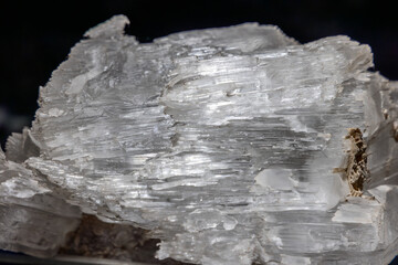Close macro of satin spar gypsum mineral, clear fibrous crystals aligned in layers showing silky texture and reflective highlights on white surface