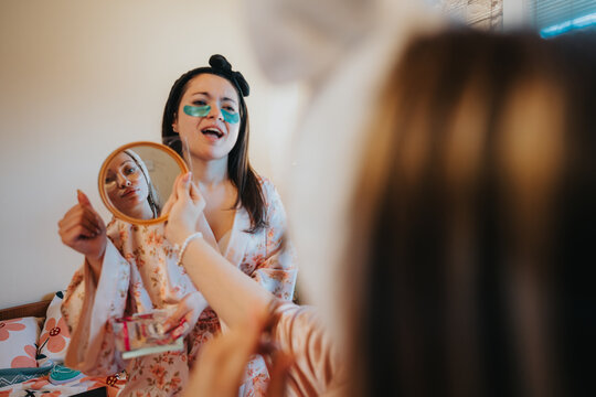 Two cheerful young women engaging in a skincare routine, applying masks and enjoying friendship.