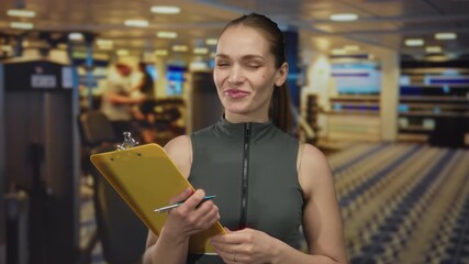 Woman with clipboard and pen gestures while discussing workout routine in a gym building; motivational support.