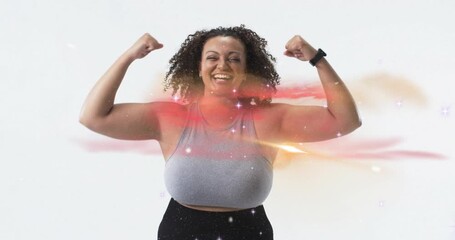 Woman tapping fitness tracker and posing bold in white studio with glowing trails showing strength