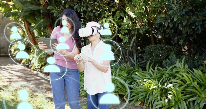 Daughter guiding mother in garden, tapping tablet and showing VR avatars with her learning motions