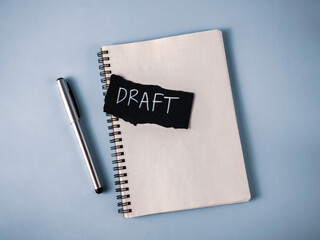 Drafting a Document Concept: Notebook, Silver Pen, and Black Paper with White 'Draft' Text for Writing and Revision