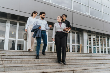 A team of business professionals descend steps outside a contemporary office structure, discussing tasks.