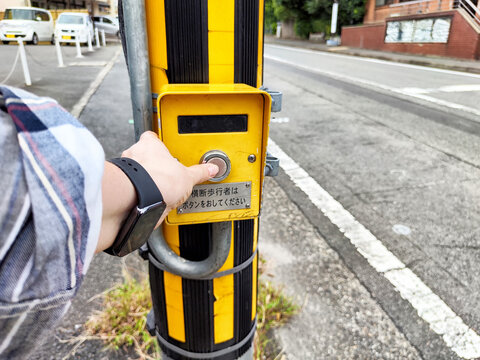 Pedestrian waits to cross the street by pressing the button at a crosswalk in a quiet urban area