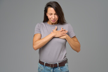 Woman holding chest with both hands and eyes closed in discomfort, studio shot