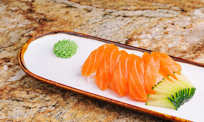 Sliced salmon sushi served on a white plate with wasabi and cucumber