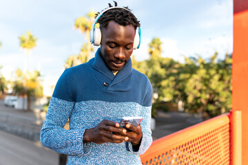 African American man using mobile phone and headphones enjoying music outdoors
