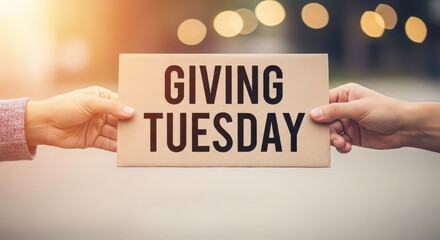 Hands holding a sign that says giving tuesday with bokeh lights in the background
