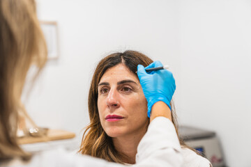 Doctor marking an adult female face for anti aging cosmetic injections to reduce facial wrinkles in...