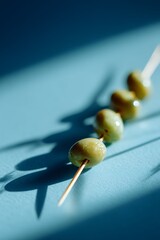 Close-up of green olives on a skewer casting shadows on blue background, highlighting texture and natural light contrast.