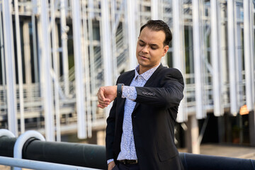 Confident latin businessman in suit checking time outdoors