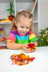 Happy little girl in a rainbow t-shirt playing with and eating colorful gummy candies or vitamins.