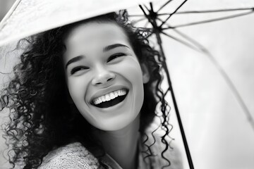 Joyful woman with curly hair laughing under an umbrella in black and white