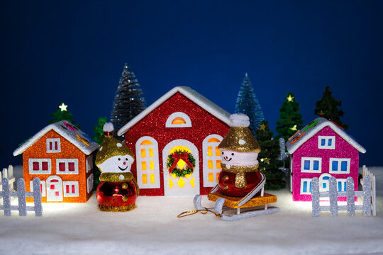 In front of three colorful houses there are snowmen on sleds and without them