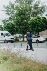 A young couple sharing an electric scooter on a city street surrounded by trees.