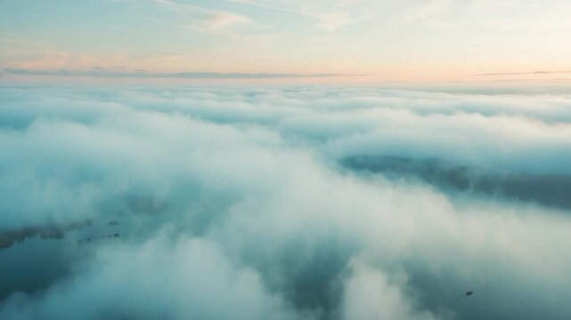 Aerial view of soft white clouds rolling over a serene lake during sunrise capturing the gentle transitions of light and shadow across the mist-covered landscape with tranquil blue and warm orange