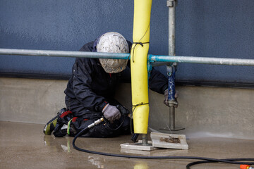 家の周囲を高圧水で洗浄する作業員