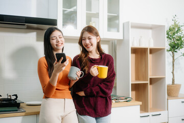 Two young Asian women enjoy breakfast together in a cozy kitchen, smiling, chatting, and sharing food