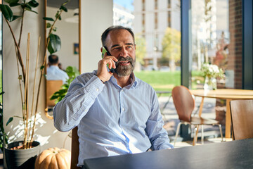 Businessman in Café Smiling While on Phone by Window With Autumn Decor and Pumpkin Accent