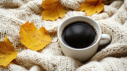 Cozy black coffee in a white cup on a knitted blanket with golden autumn maple leaves
