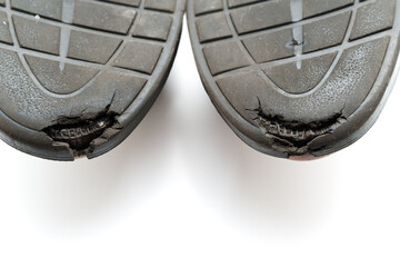 Old shoes with worn out soles resting on a white surface