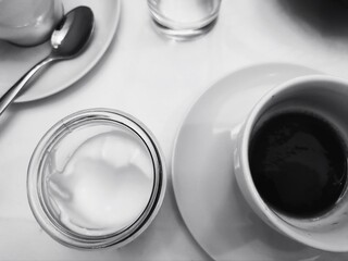Morning Coffee and Cream. Black and white composition featuring a cup of coffee, a small container of cream, and a teaspoon on a white surface. The overhead view creates a minimalist, geometric layout