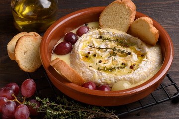Baked camembert or  brie cheese with honey, grapes, aromatic herbs and crusty bread