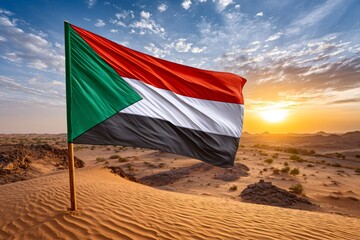 Sudan flag flying over desert sand dune at sunset