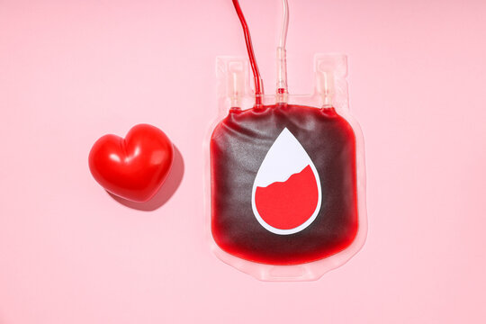 Red blood bag with drop symbol and heart on a pink surface