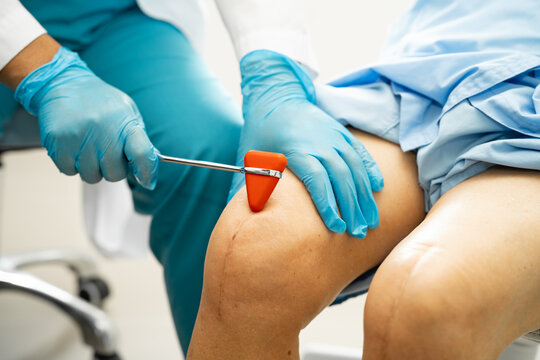 Asian doctor physiotherapist examining, massaging and treatment knee and leg of senior patient in orthopedist medical clinic nurse hospital.