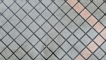 A close-up view of square pavement tiles arranged in a diagonal grid, featuring rough textured surfaces with alternating gray and muted orange tones. The tile floor is wet and damp after the rain.