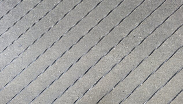 Close-up shot of rough gray concrete surface, showing clear gravel and sand texture. Features diagonal grooves for anti-slip safety. Ideal for backgrounds, architectural concepts, or walkways.