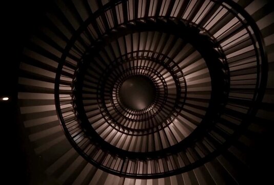 Dramatic low angle view reveals architectural elegance of circular staircase with contrasting light and shadow in motion
