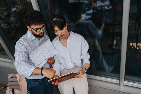 Two business colleagues analyze financial charts and reports outside, conveying teamwork and collaboration.