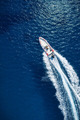 Aerial overhead view of a RIB speedboat crossing the turqoise ocean with speed and leaving a trail of waves and surf
