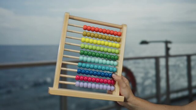 Man holding colorful abacus on a seaside cruise boat outdoors against ocean backdrop, emphasizing outdoor activities and creative learning tools at sea.