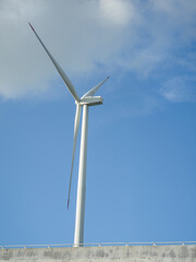 Tall wind turbine spinning against a clear blue sky on a sunny day near the coast