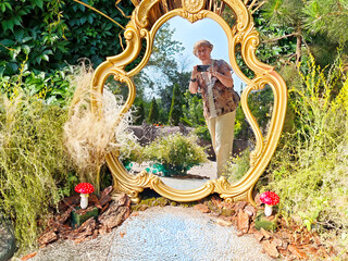Mature woman blogger takes a cheerful selfie in a beautiful garden with reflections and nature