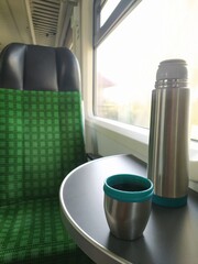 Interior train carriage showcasing table with modern thermos, teacup against landscape visible through the window