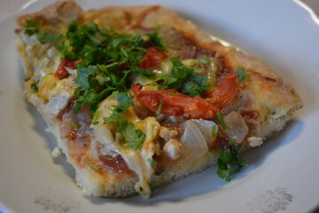 Food, groceries, homemade fresh baked goods. A large slice of pizza with chicken pieces, tomato slices, cheese, and fresh herbs sits on a ceramic plate.