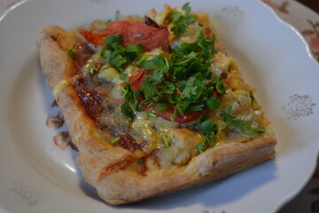 Food, groceries, homemade fresh baked goods. A large slice of pizza with chicken pieces, tomato slices, cheese, and fresh herbs sits on a ceramic plate.