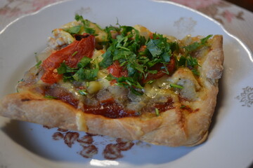 Food, groceries, homemade fresh baked goods. A large slice of pizza with chicken pieces, tomato slices, cheese, and fresh herbs sits on a ceramic plate.