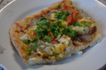 Food, groceries, homemade fresh baked goods. A large slice of pizza with chicken pieces, tomato slices, cheese, and fresh herbs sits on a ceramic plate.