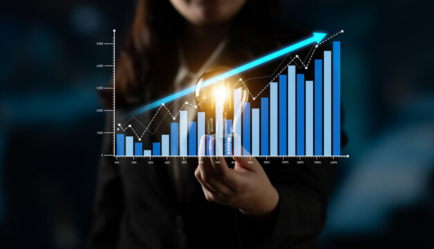 Businesswoman presents a glowing light bulb while standing beside a financial graph, illustrating growth trends and innovative ideas in a corporate environment. Scalp - Powered by Adobe